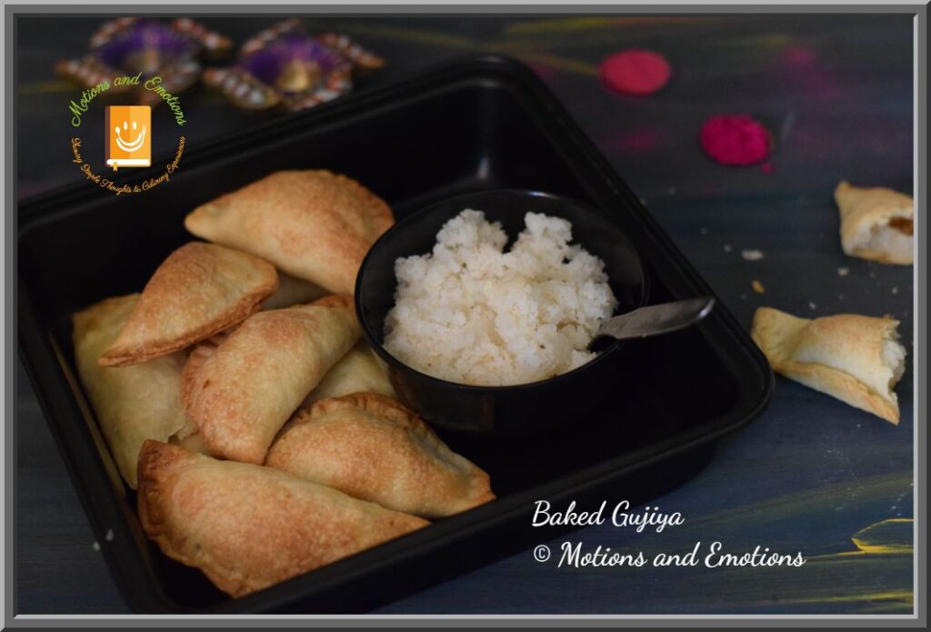 Baked Gujiya in black baking tray along with coconut stuffing in a black bowl with spoon and one broken gujiya