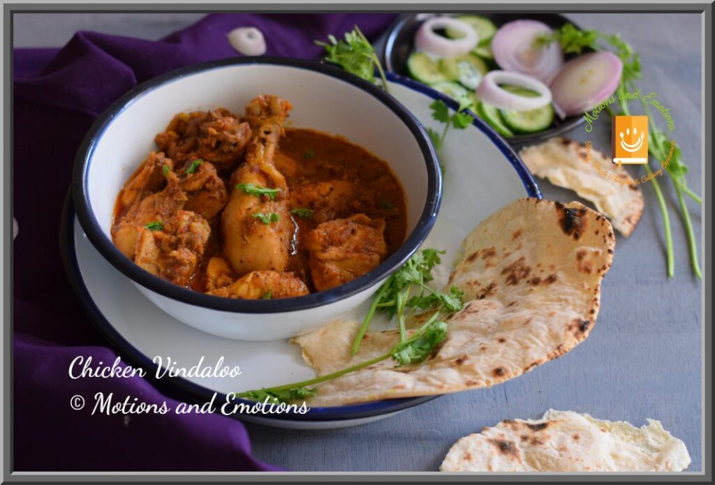 Goan Chicken vindaloo served in a white bowl on top of a white plate along with naan and salad