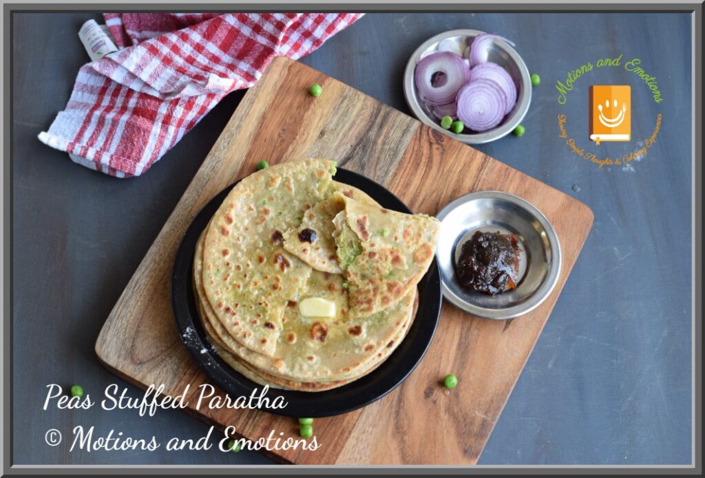 Top view of Peas Paratha with a dollop of butter served in a black plate with pickle and onion 