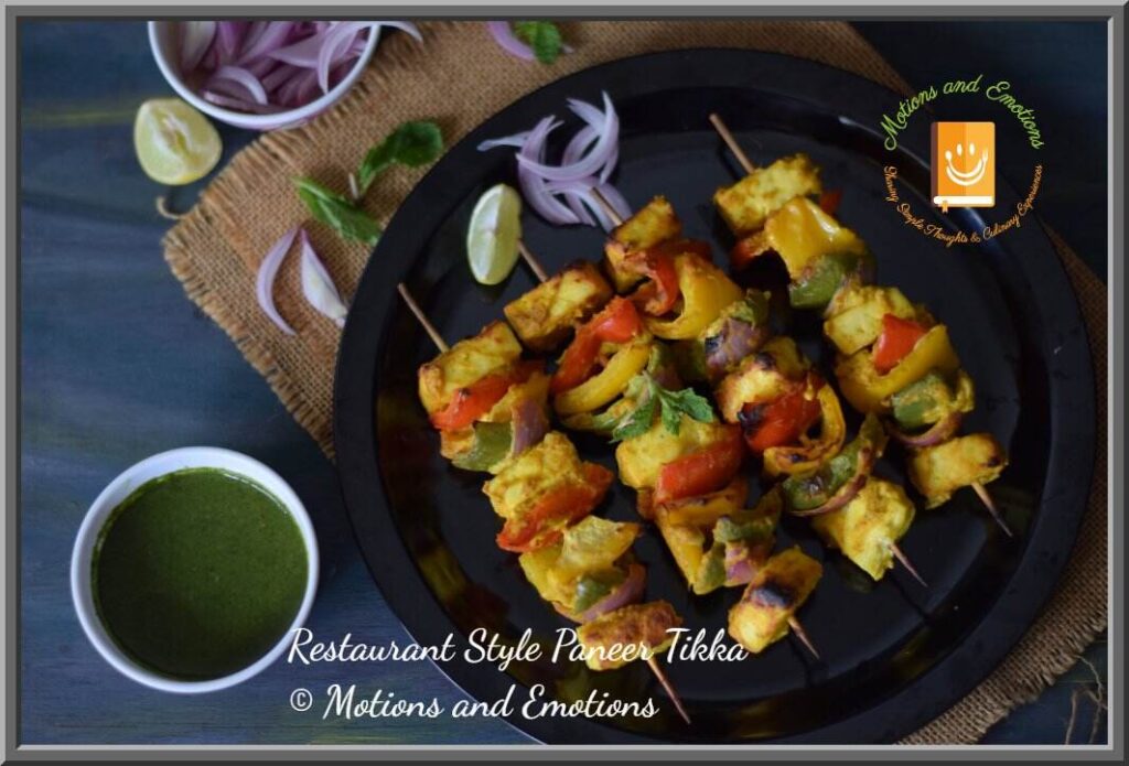 Paneer tikka skewers served on a black plate along with green chutney , top view