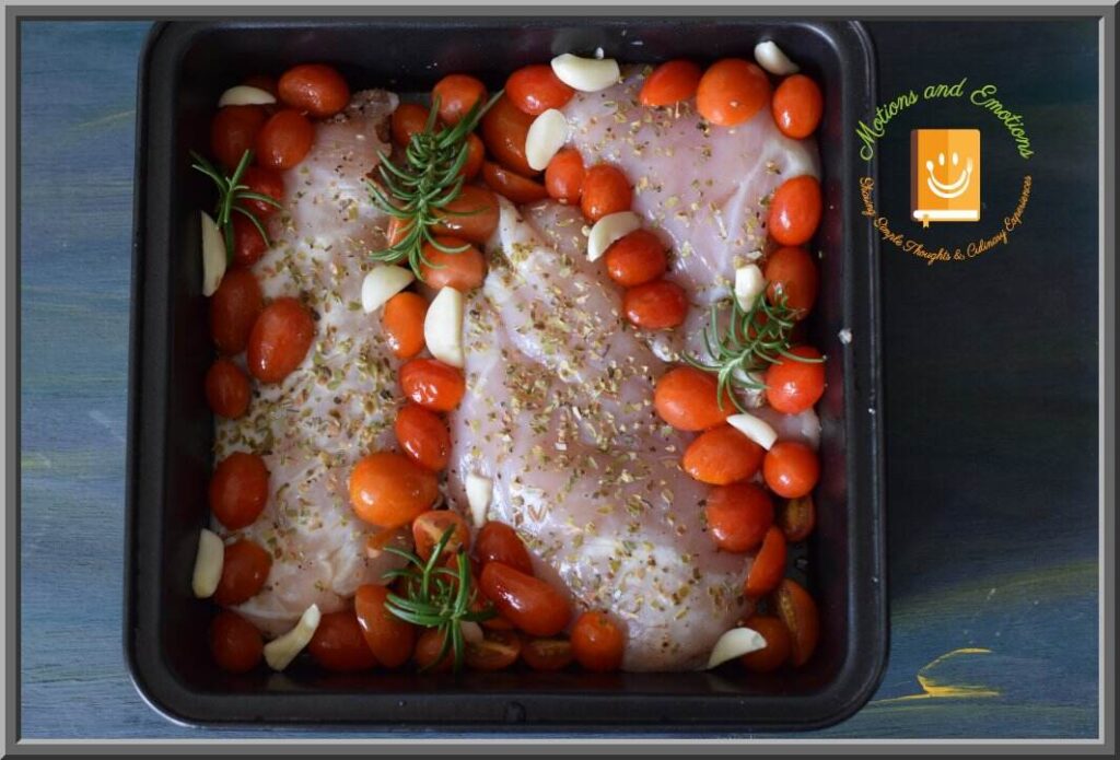Marinated chicken breasts along with cherry tomatoes and garlic placed in a black baking tray