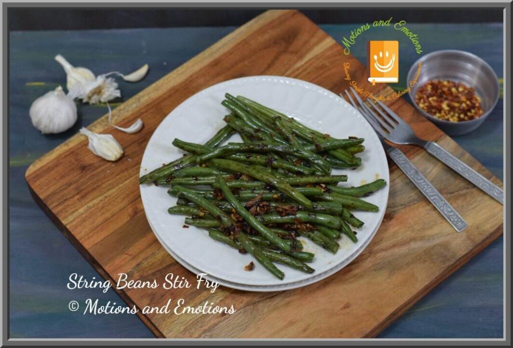 String beans stir fry served on white plate along with forks garlic chilli flakes