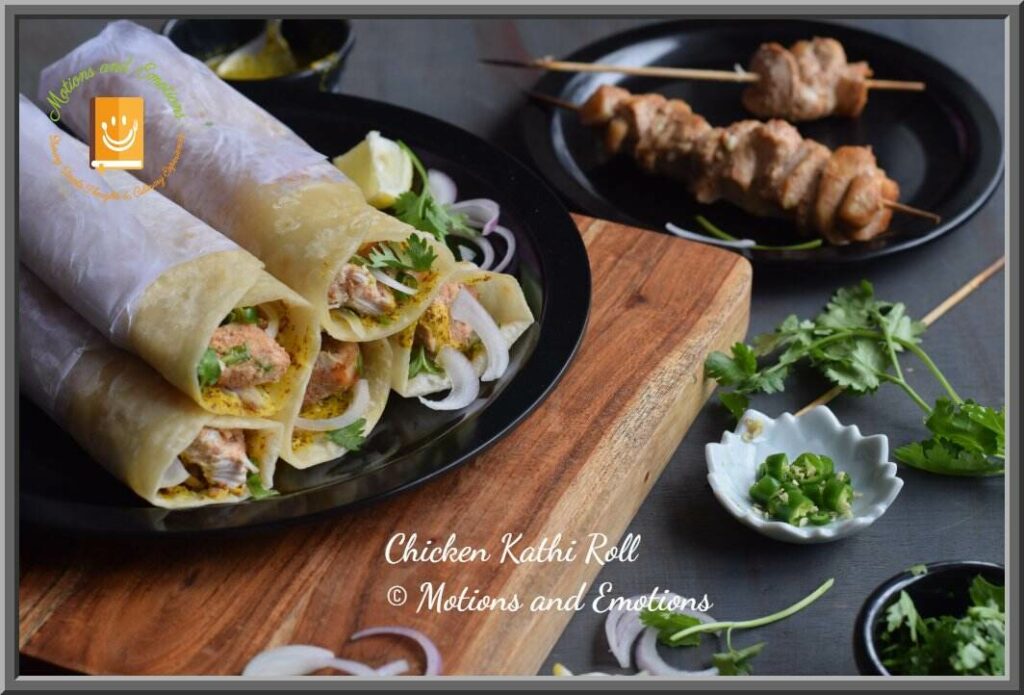 Chicken roll stacked on a black plate, chicken skewers and onion, coriander leaves