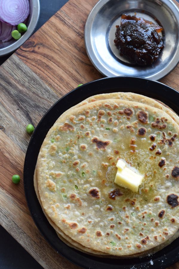 Stack of Peas Paratha with a dollop of butter served in a black plate with pickle and onion