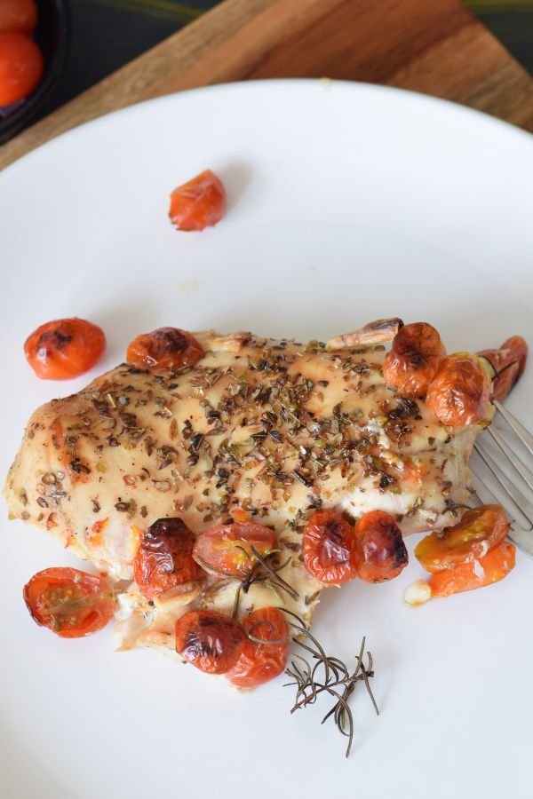 Baked chicken with cherry tomatoes and herbs served on a white plate