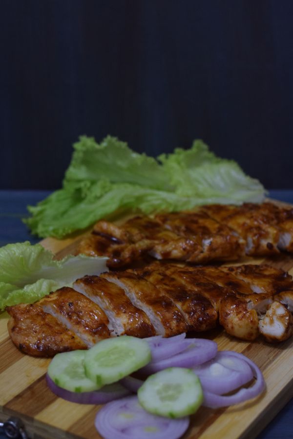 sliced bbq chicken breasts with salads on wooden board