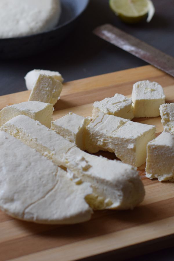 Paneer cubes cut from paneer block scattered on wooden board along with knife and lemon