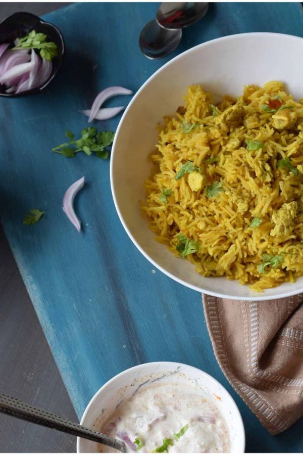 Egg Bhurji Pulao served in a white bowl along with raita and sliced onions
