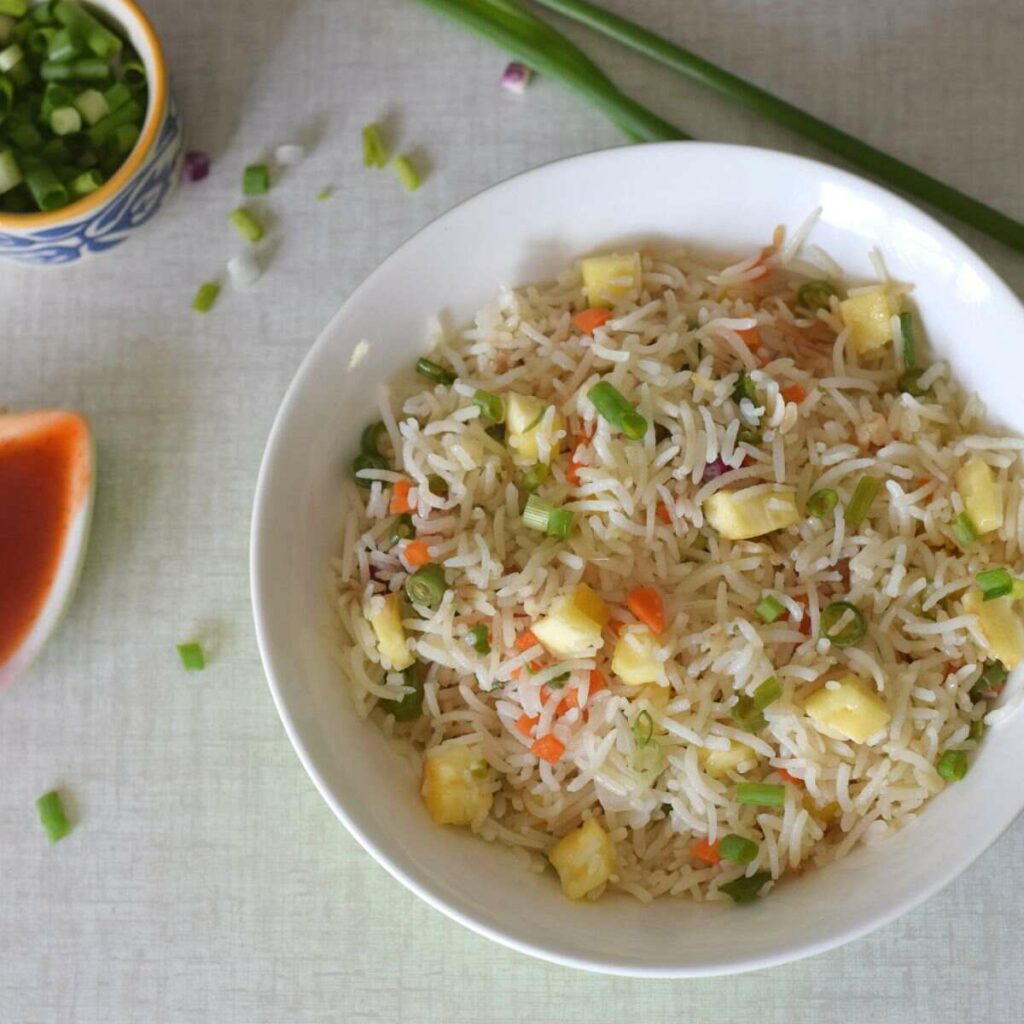 A bowl of paneer fried rice along with ketchup and chopped spring onions