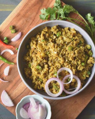 A bowl full of egg tadka along with raw onion, green chilli and coriander leaves