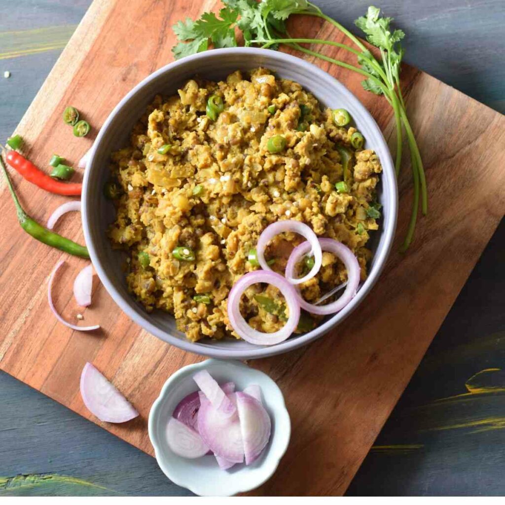Bowl full of tadka dal kept on wooden board along with raw onion chilli and coriander leaves