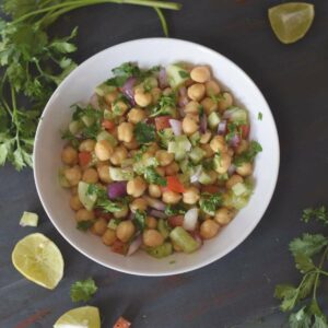 A bowl full of chickpea salad along with lemon, coriander leaves on the background
