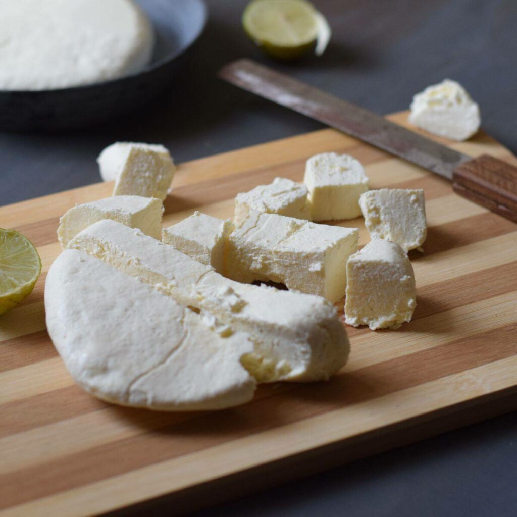 paneer pieces on wooden board along with knife and lemon in the background
