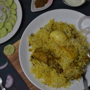 chicken biryani on a white plate along with salad