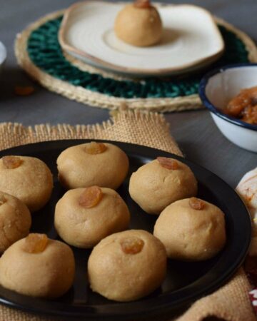 nolen gurer sondesh served on a black plate along with a sondesh served in a saucer and jaggery in the background