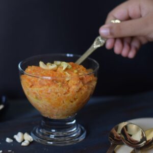 Digging Gajar ka halwa with a golden spoon from a dessert bowl; Side view
