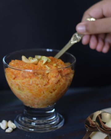 Digging Gajar ka halwa with a golden spoon from a dessert bowl; Side view