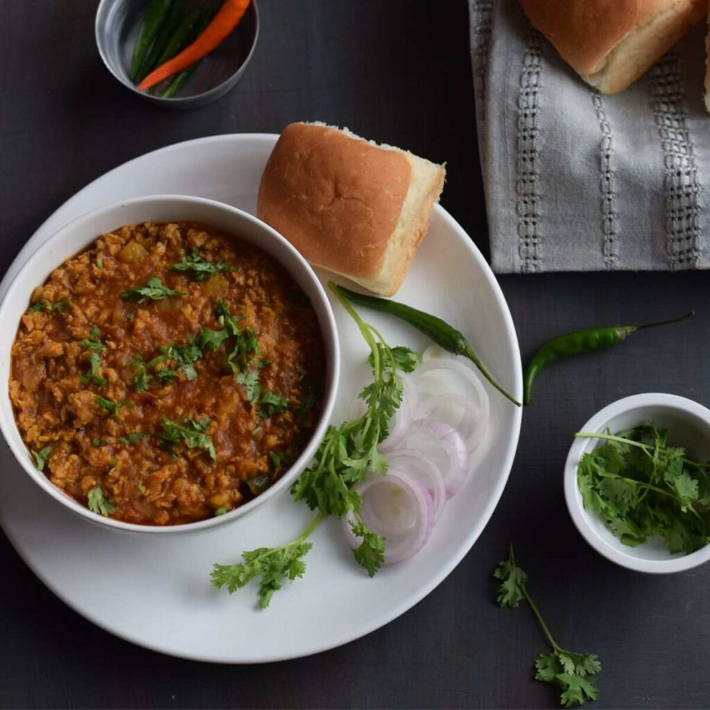 a bowl full of chicken keema masala with pav, sliced onions and coriander leaves