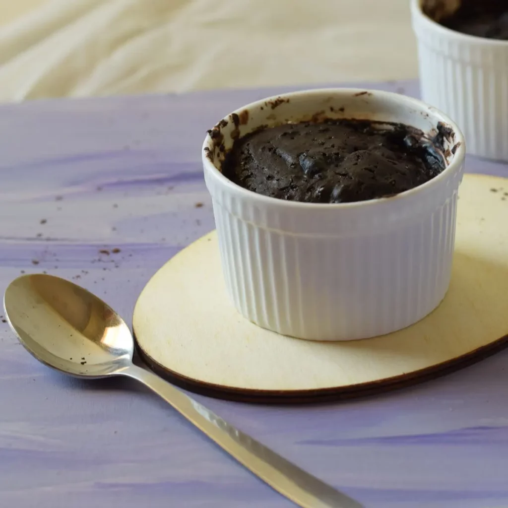 chocolate mug cake in ramekin on a wooden board along with a spoon