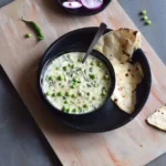 methi matar malai in a bowl along with naan bread in black plate, onion slices and peas in the background