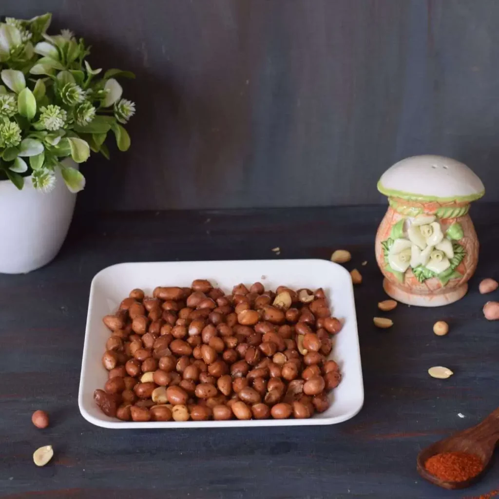 spicy peanuts in square plate along with artificial plant and scattered peanuts and spices