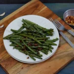 String beans stir fry served on white plate on top of wooden board