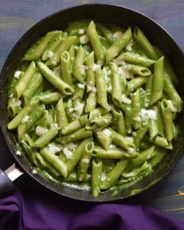 a pan full of green sauce pasta along with a blue cloth in the background