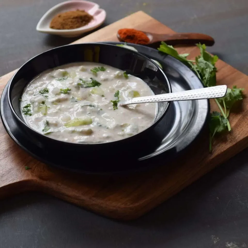 raita in a black bowl kept on black plate and wooden board in the background