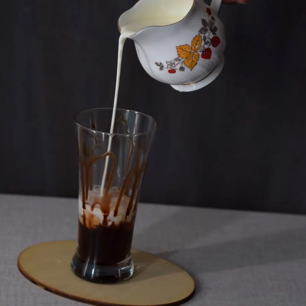milk pouring in coffee decoction in a tall glass