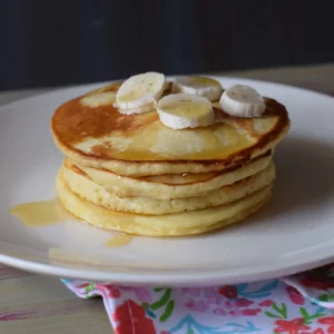 stack of pancakes on white plate topped with banana