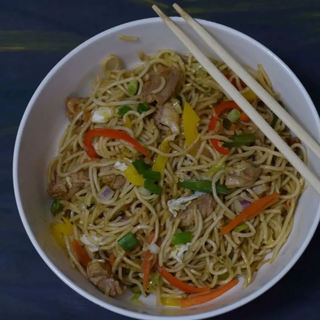 A bowl of chicken noodles with chopsticks