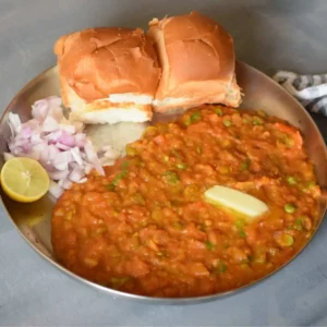 Pav Bhaji served on a steel plate with a dollop of butter, chopped onion and lemon wedge