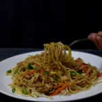 taking chicken hakka noodles with a fork from white plate