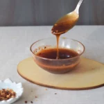 taking a spoon of honey hot sauce from a glass bowl