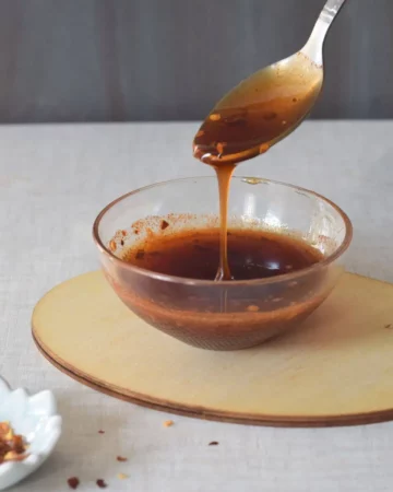 taking a spoon of honey hot sauce from a glass bowl