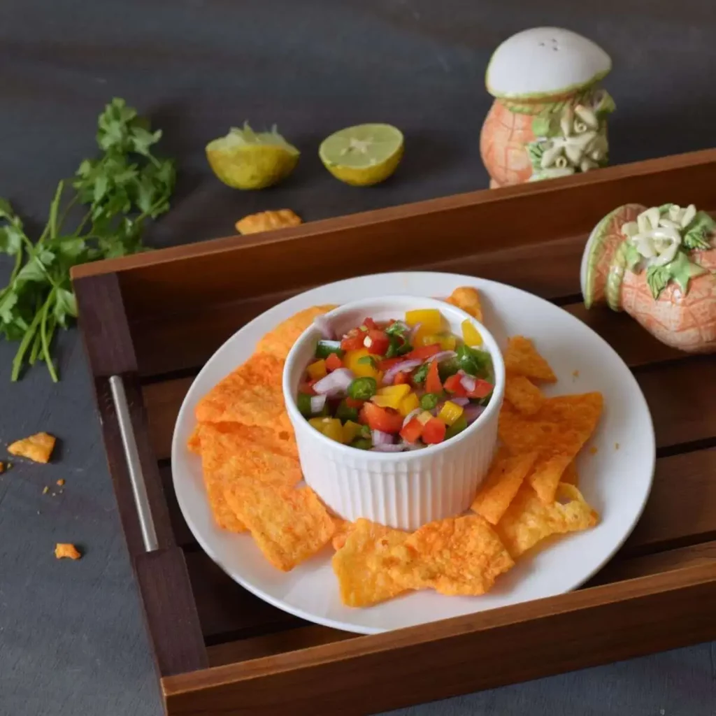 salsa in a ramekin along with nachos on a wooden tray and coriander leaves lemon in the background