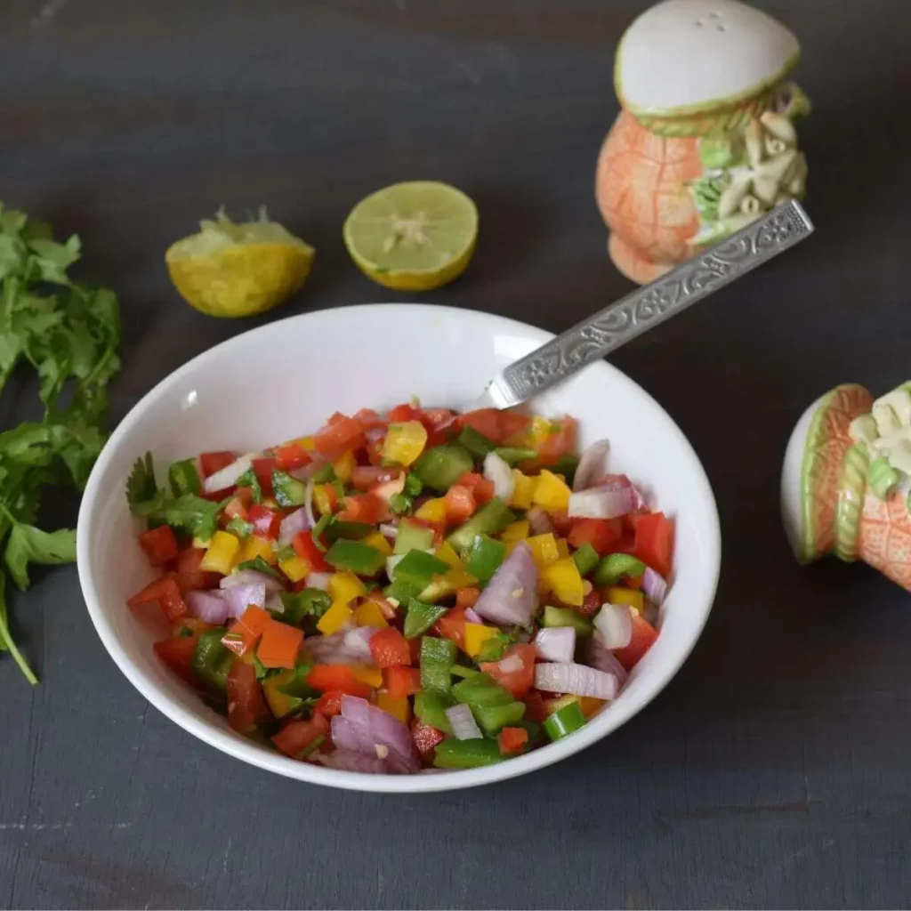 bell pepper salsa in a white bowl along with lemon, coriander leaves in the background