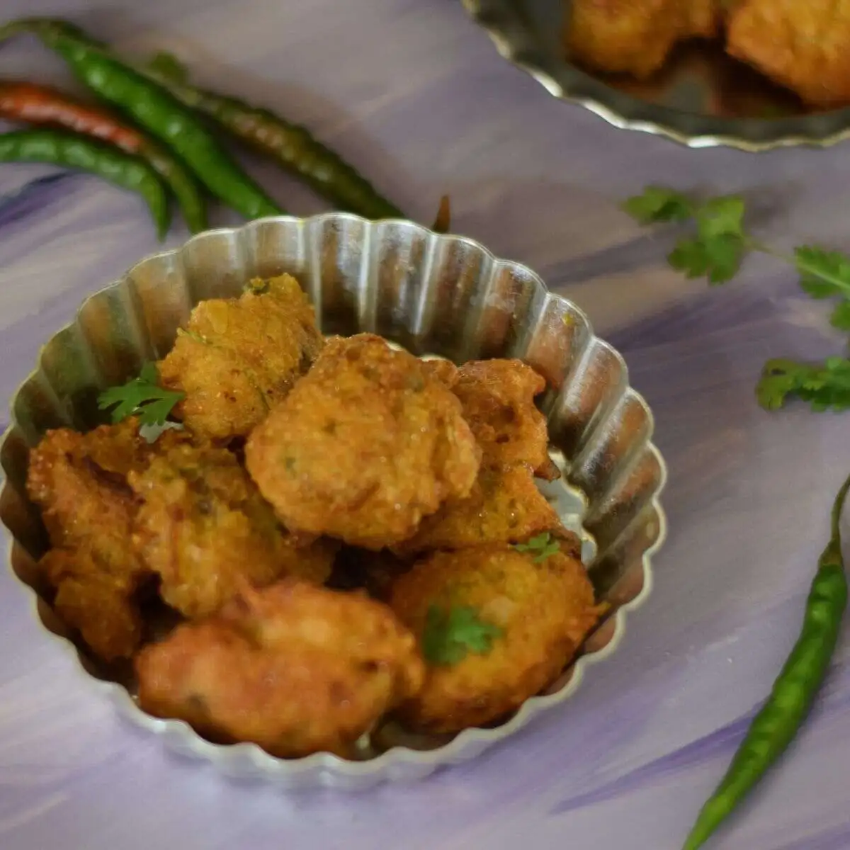 Fish roe fritters served on a plate along with green chilli and coriander leaves