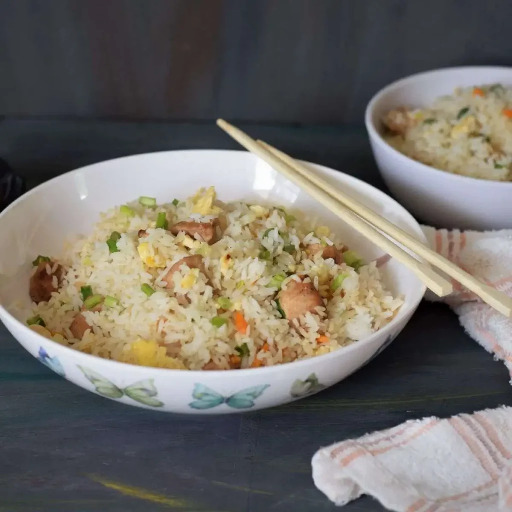 Chicken fried rice in a white bowl along with chopsticks