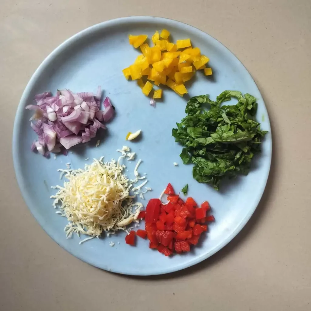 Chopped onion, bell peppers, spinach and grated cheese in a plate