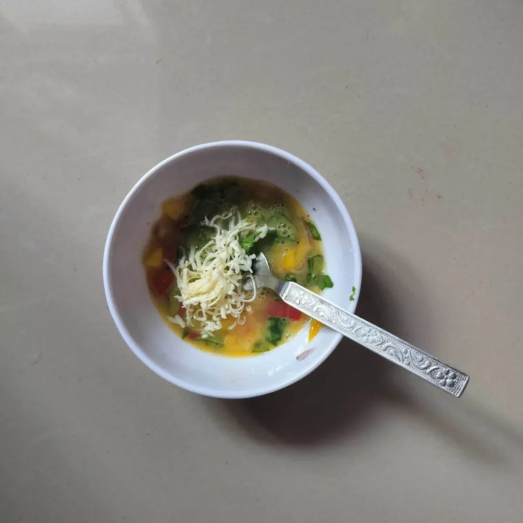 Beaten egg along with vegetables and grated cheese in a bowl and fork