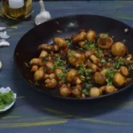spicy garlic mushroom in a nonstick pan and garlic coriander leaves in the surrounding