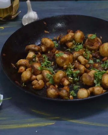 spicy garlic mushroom in a nonstick pan and garlic coriander leaves in the surrounding