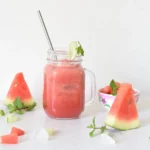 juice in a mason jar along with piece of watermelon and mint scattered