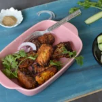 fish tikka in a pink tray along with cucumber, onion, coriander leaves and spices