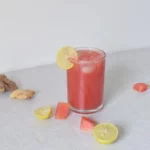 watermelon ginger juice in a small glass along with lemon watermelon cubes and ginger